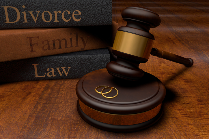 Stack of three gray textbooks with the words "divorce," "family" and "law" written in gold print. The textbooks are behind a wooden gavel that is poised above two golden rings.
